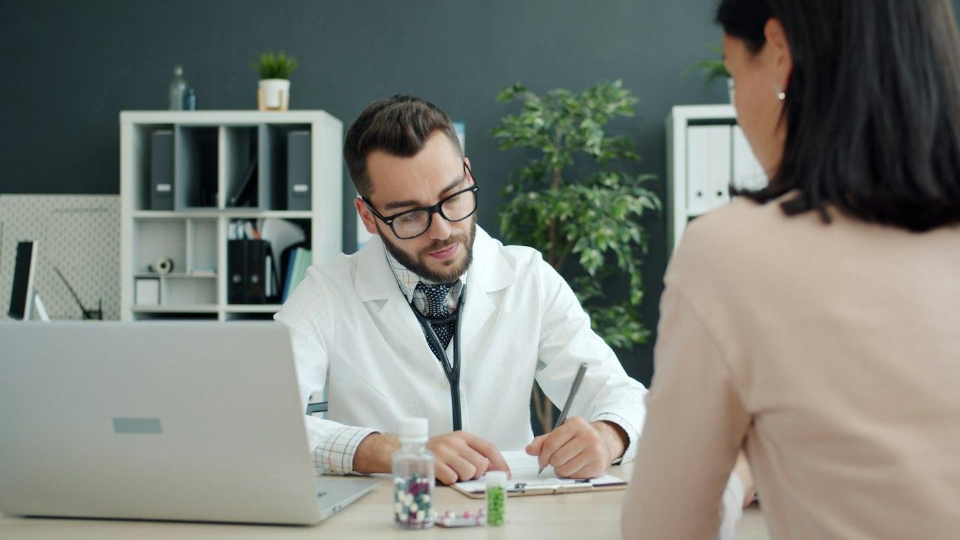 A doctor writing notes while a patient sits opposite